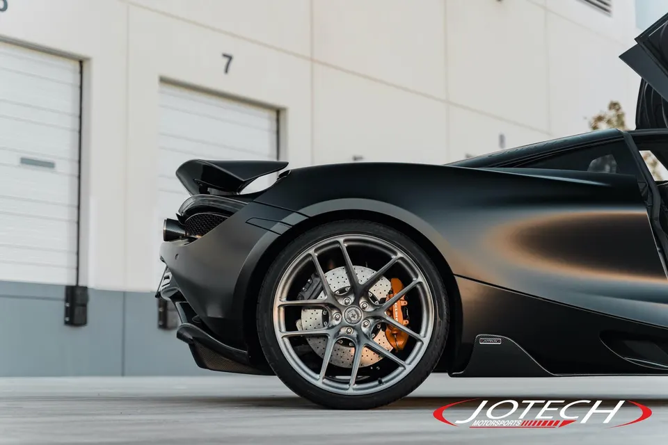 Black McLaren 720S with aftermarket multi-spoke wheels, orange brake calipers, and carbon fiber rear wing.