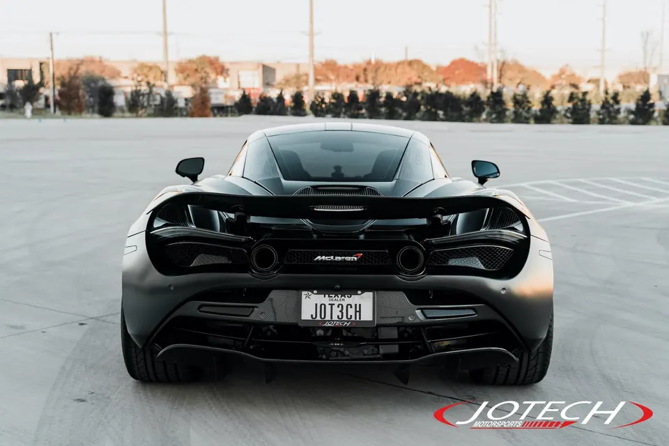 A matte black McLaren 720S supercar from the rear, showcasing its active wing, diffuser, and dual exhaust tips.