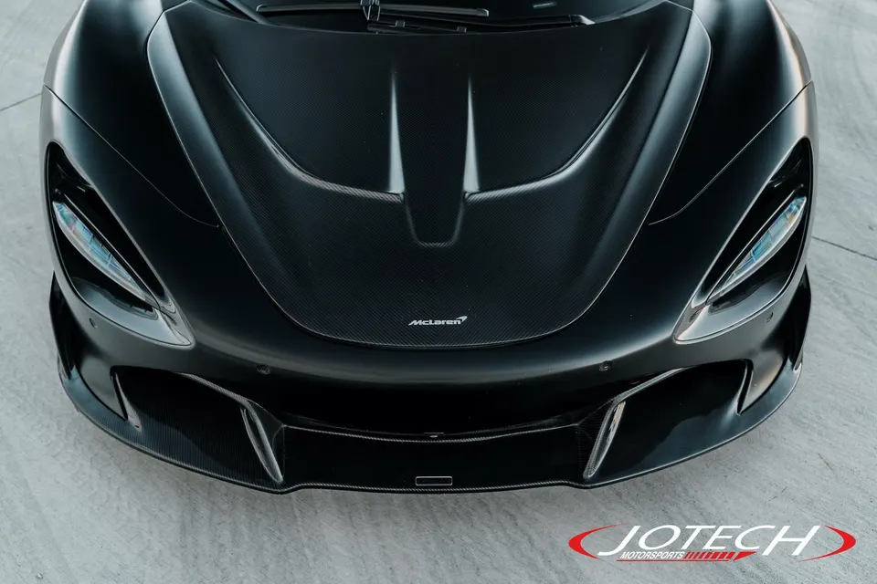 Close-up of a black McLaren's carbon fiber hood and front bumper, showcasing its sleek design.