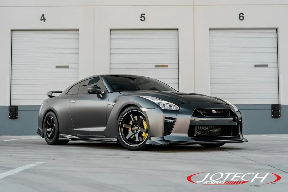 Grey Nissan GT-R with aftermarket wheels and yellow brake calipers parked in front of garage doors.