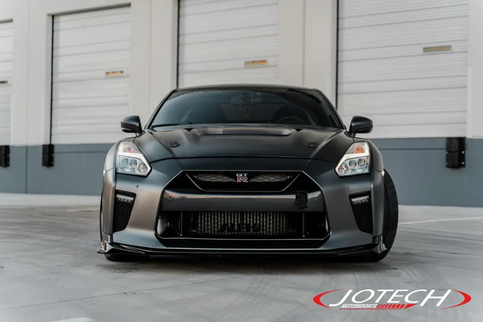 Front view of a matte grey Nissan GT-R with an aftermarket intercooler parked in front of garage doors.