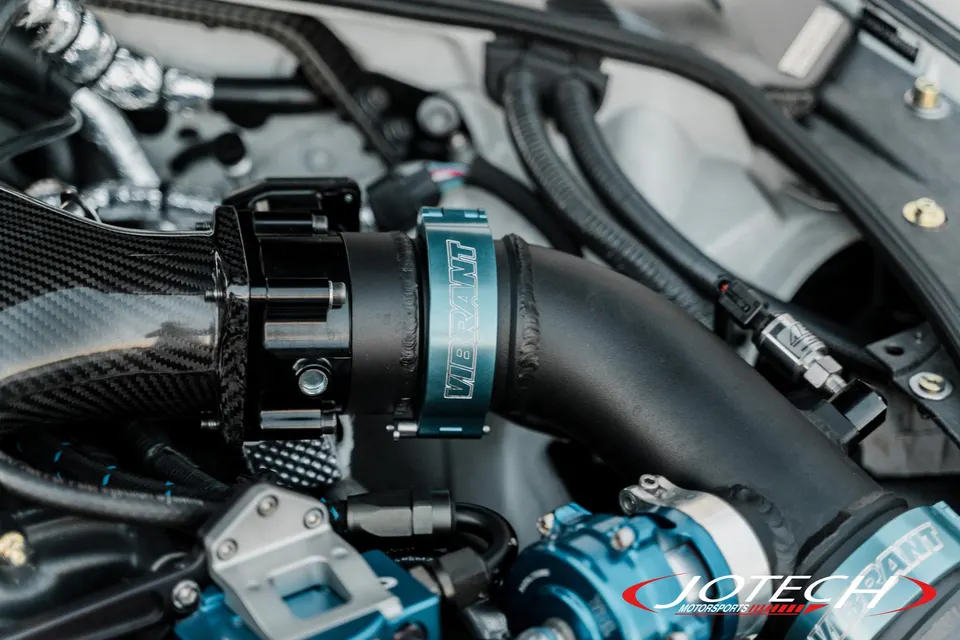 Close-up of a high-performance engine bay featuring a carbon fiber intake, boost piping, and Vibrant clamps.