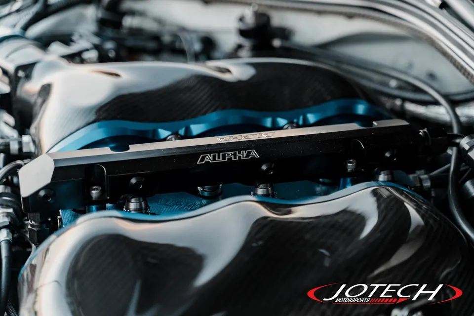 Close-up of a high-performance engine bay featuring a carbon fiber intake manifold and an Alpha fuel rail.
