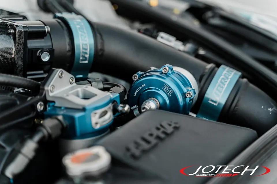 A close-up of a blue Tial blow-off valve and Vibrant clamps in a high-performance car's engine bay.