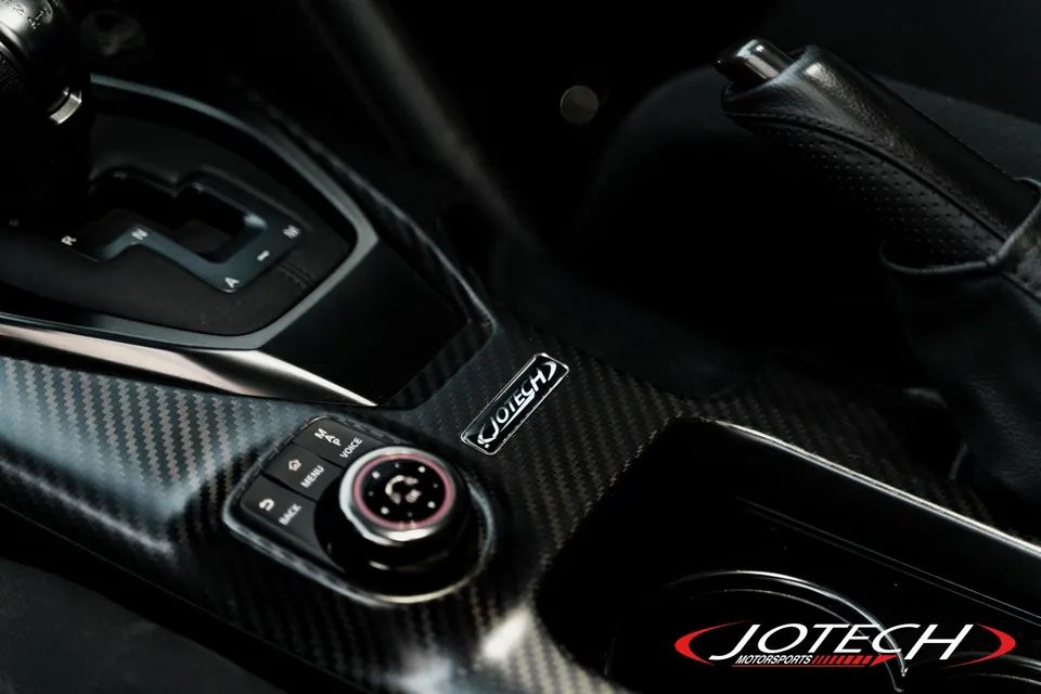 A close-up of a car's interior featuring carbon fiber trim on the center console, shifter, and infotainment controls.