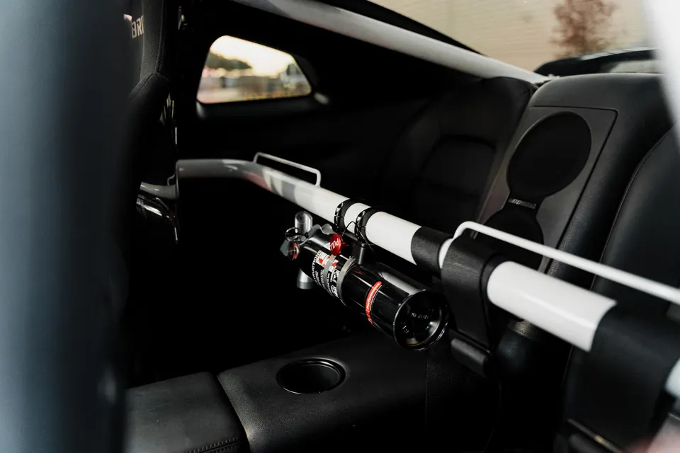 Interior view of a performance car showing a white roll bar with black stripes and a mounted fire extinguisher.