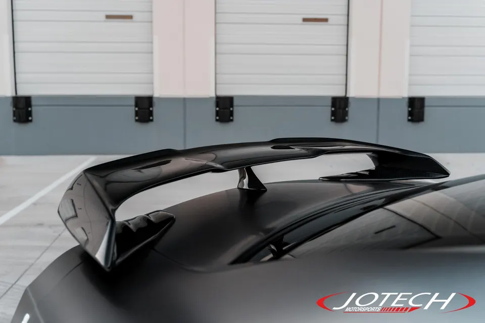 Close-up of a black car's carbon fiber rear wing, showcasing exterior aerodynamics by Jotech Motorsports.