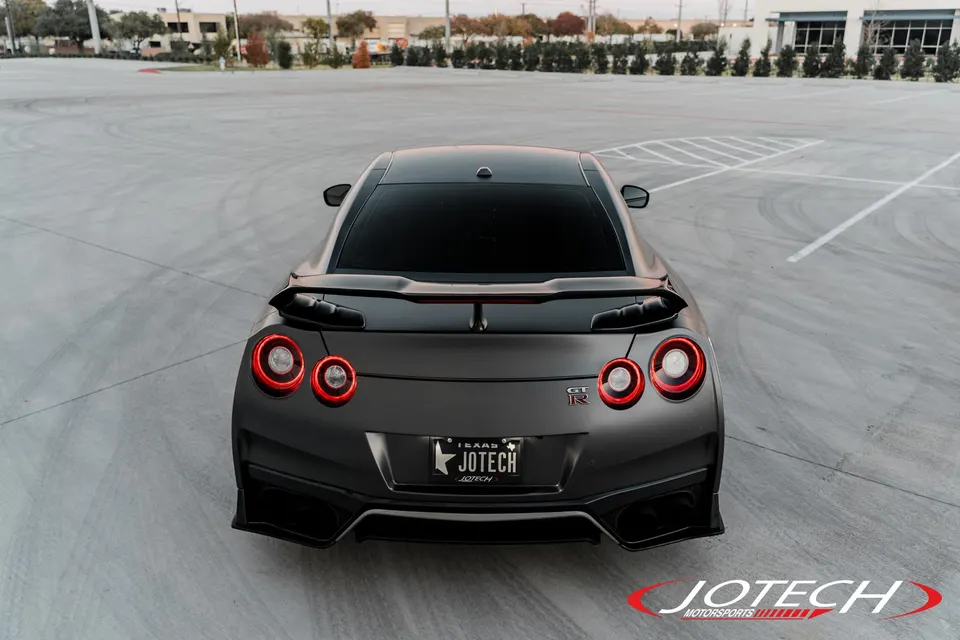 Rear view of a dark grey Nissan GT-R R35 with a custom spoiler and diffuser, parked in an empty lot.