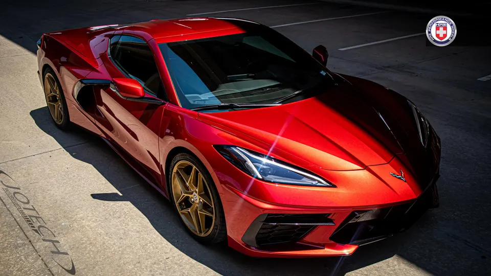 A red Chevrolet Corvette C8 with gold HRE wheels parked in a lot, showcasing its sleek design.