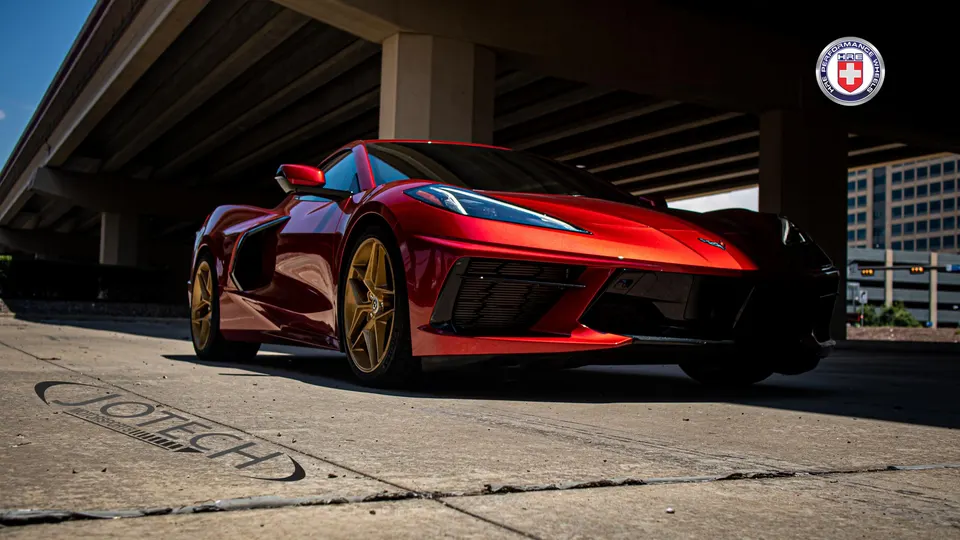 Red Chevrolet Corvette C8 with gold HRE Performance wheels parked under an overpass, showcasing its sleek design.
