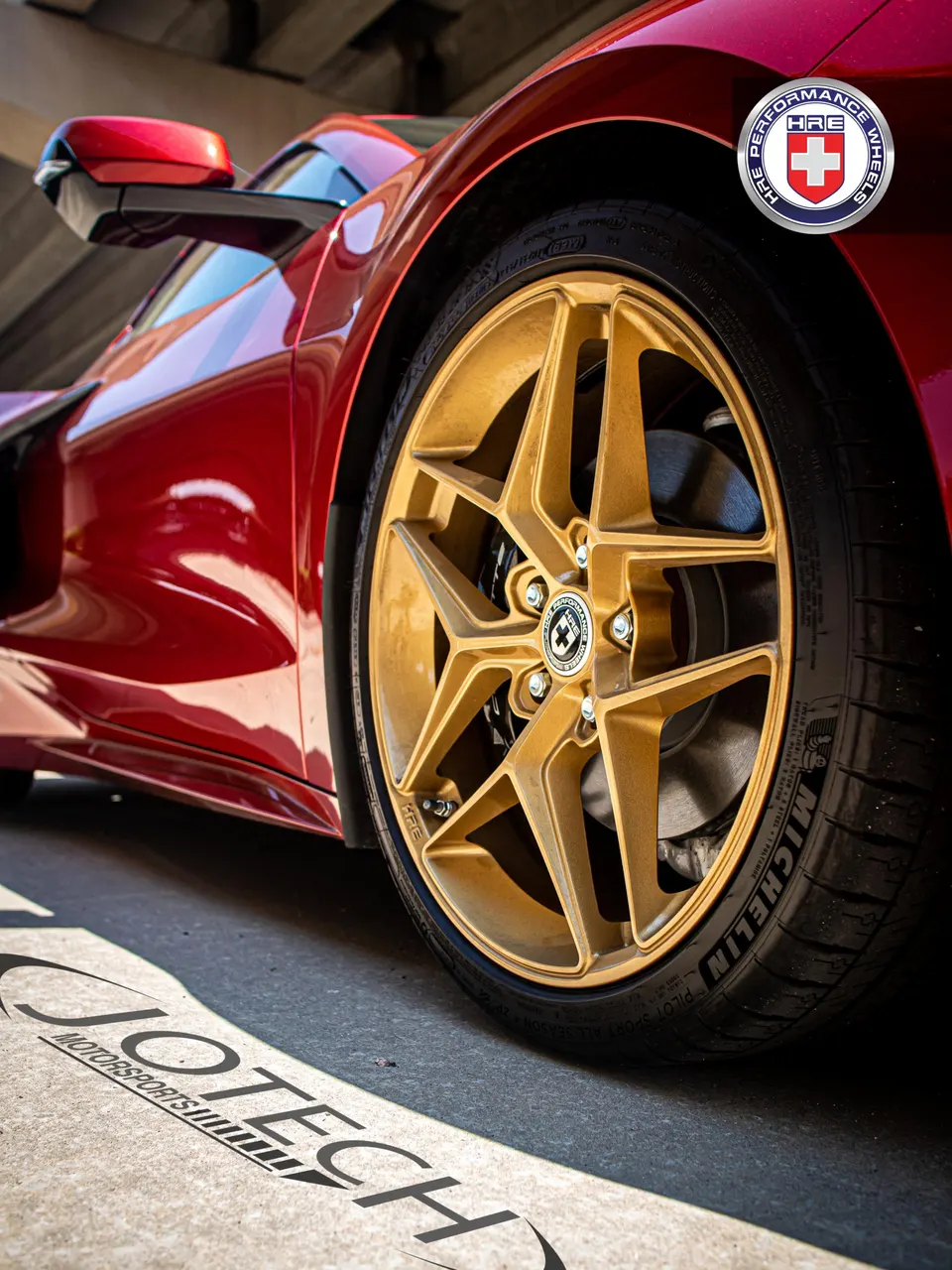 Close-up of a red C8 Corvette's gold HRE wheels and Michelin tires, highlighting the car's custom setup.