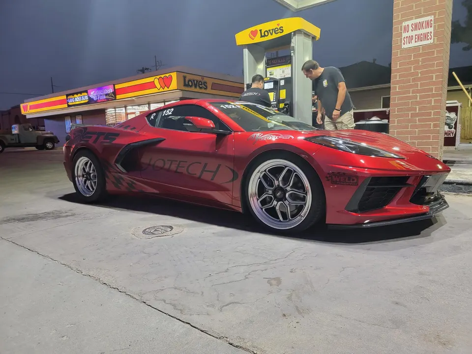 Red C8 Corvette with aftermarket wheels at a Love's gas station at night, with two men nearby.