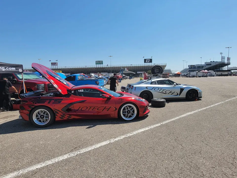 Red Corvette C8 and silver Nissan GT-R race cars from Jotech Motorsports parked at a drag strip paddock.