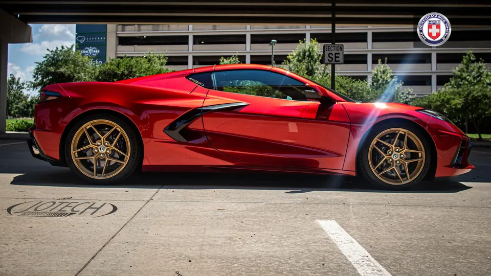 Red C8 Corvette with gold HRE performance wheels parked outdoors in a professional photoshoot setting.