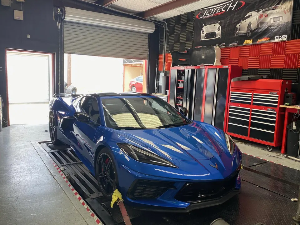 A blue C8 Corvette strapped to a dynamometer in a performance tuning shop, ready for tuning.