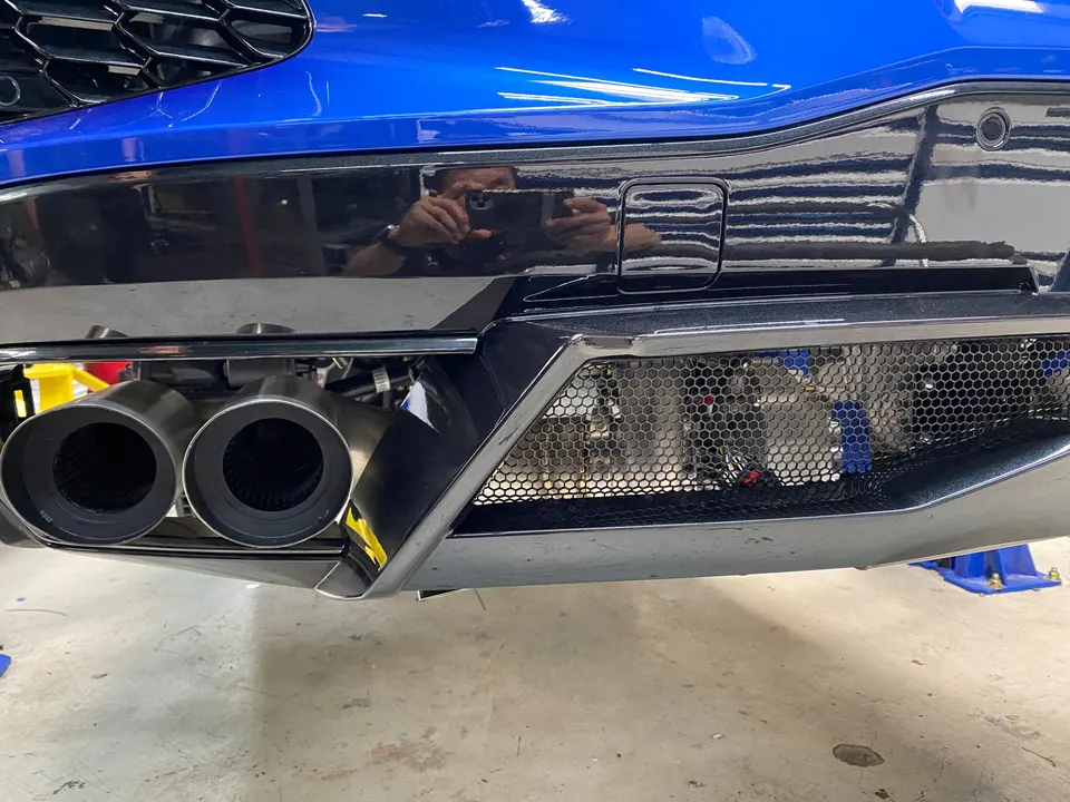 Close-up of a blue Lamborghini Huracan's performance exhaust system and rear bumper in a shop.