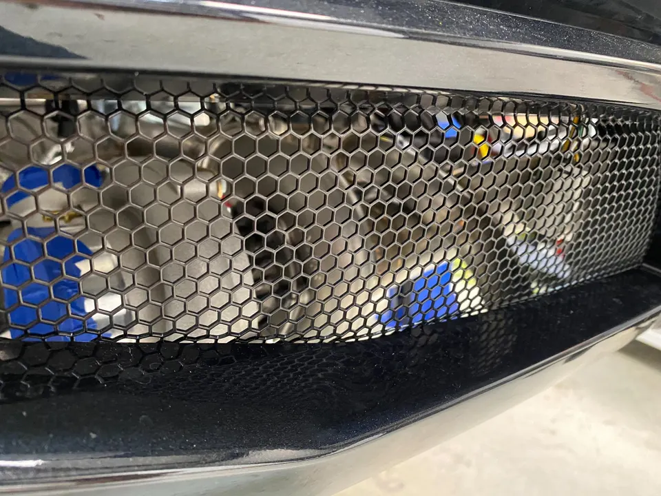 Close-up of a car's front grille with a honeycomb mesh, revealing an intercooler and blue hoses behind it.