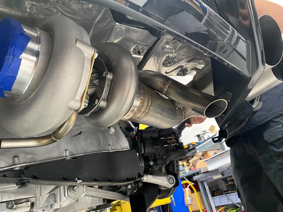 Close-up of a large turbocharger and custom exhaust system being installed on a performance car at a tuning shop.