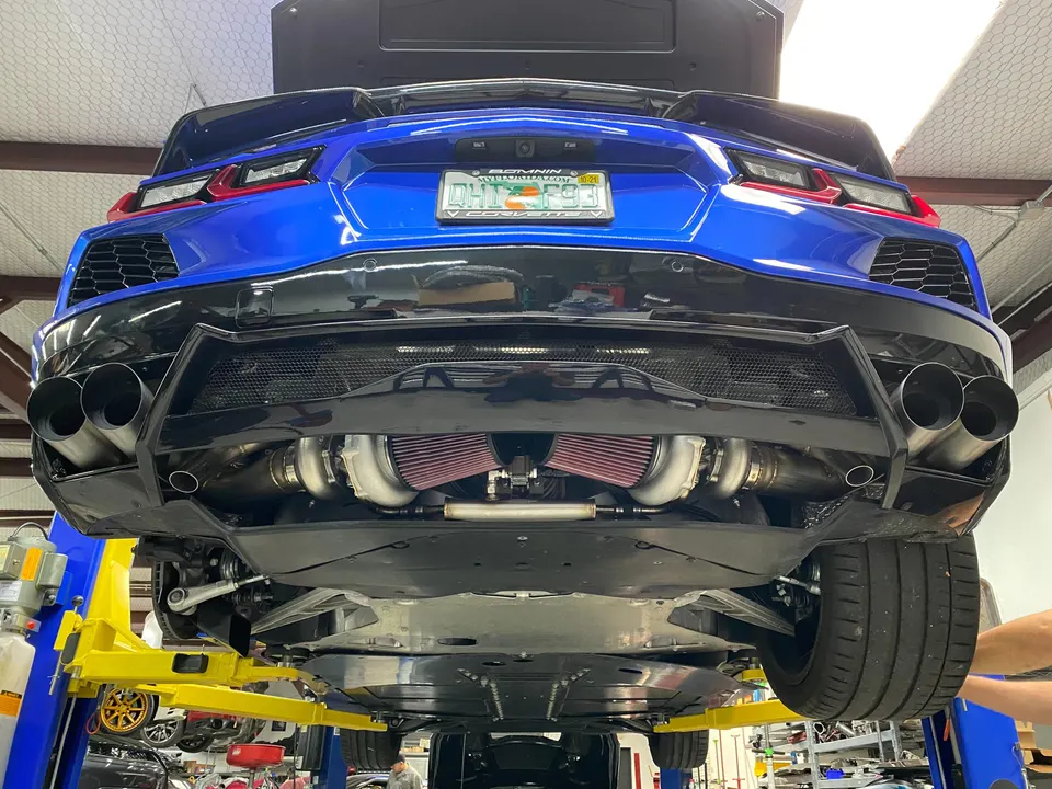 A blue C8 Corvette on a lift in a shop, showcasing its twin turbochargers and custom exhaust system.