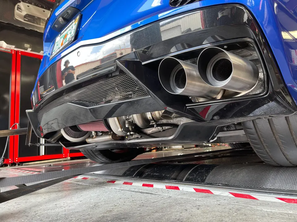 Rear view of a blue C8 Corvette on a dyno, showcasing aftermarket exhaust tips, turbochargers, and a performance air filter.