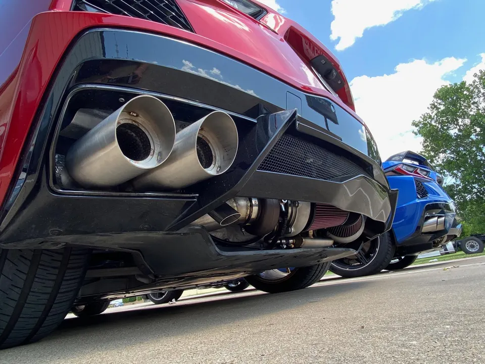 A close-up of the rear of a red C8 Corvette, showcasing its custom exhaust system and visible turbocharger setup.