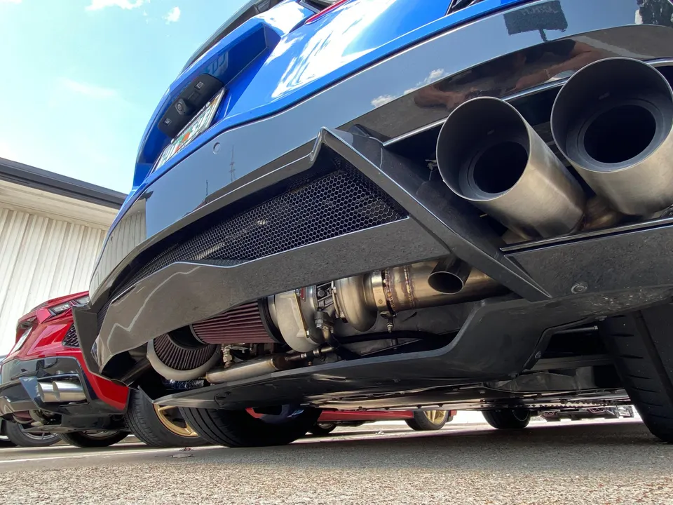 Rear view of a blue performance car showcasing custom exhaust tips, a visible turbocharger, and an aftermarket air filter.