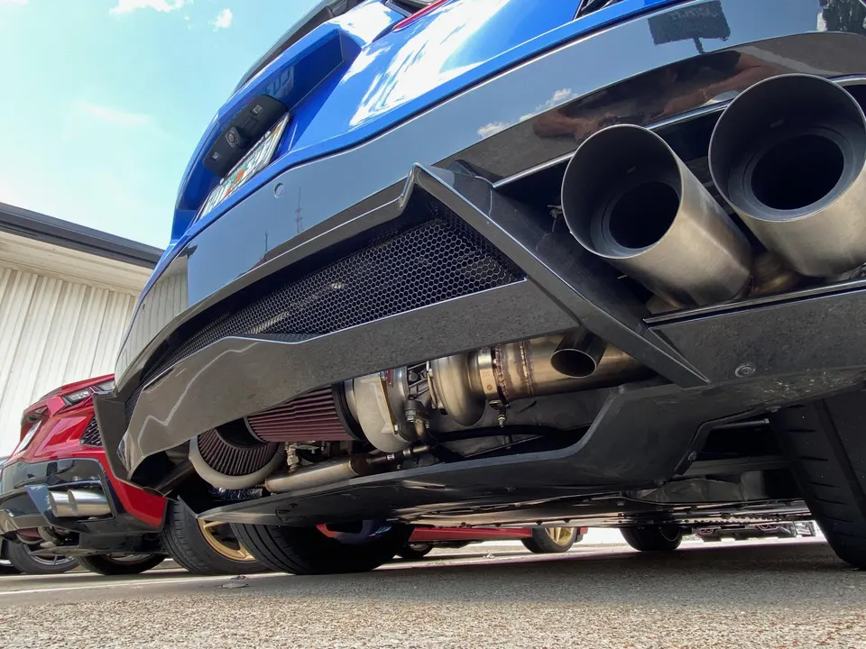 Close-up of a blue car's rear undercarriage showcasing a turbocharger, custom exhaust, and diffuser.