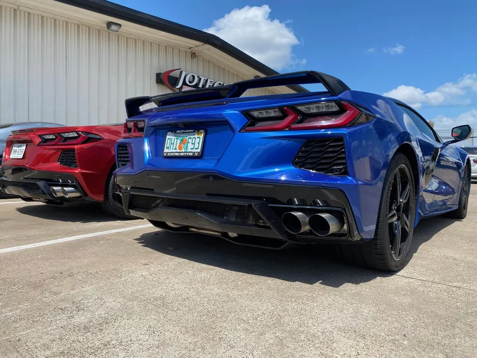 Rear view of a blue Chevrolet C8 Corvette with a large wing and a red C8 Corvette parked outside Jotech Motorsports.