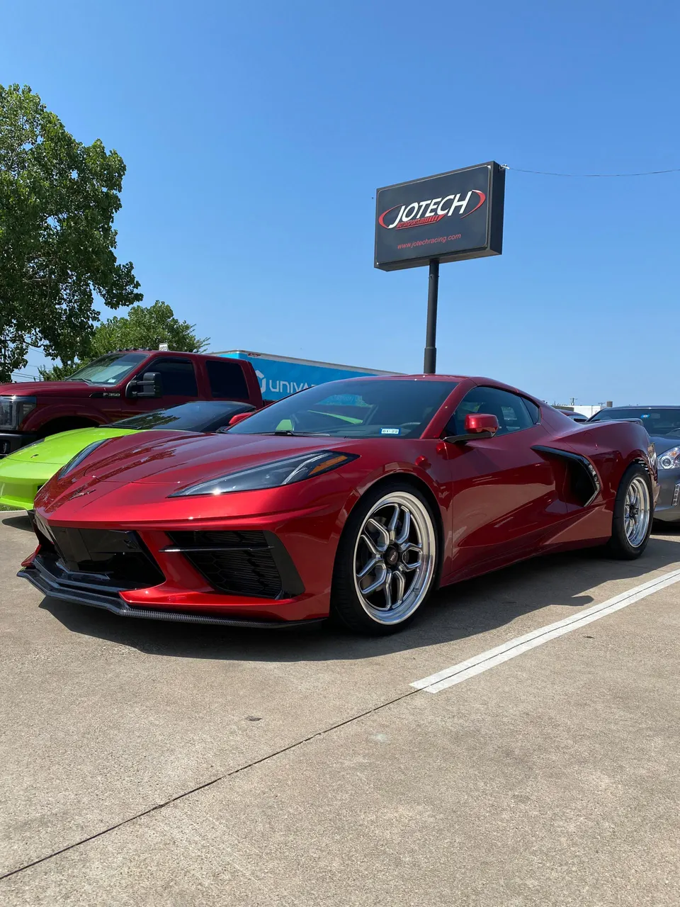 Red Corvette C8 with aftermarket wheels and carbon fiber splitter parked outside Jotech Motorsports performance shop.