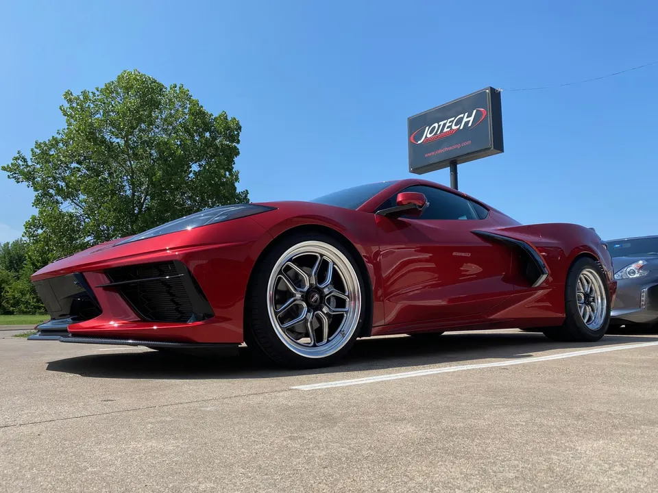 Red Corvette C8 with aftermarket wheels and front splitter parked in front of Jotech Motorsports sign.