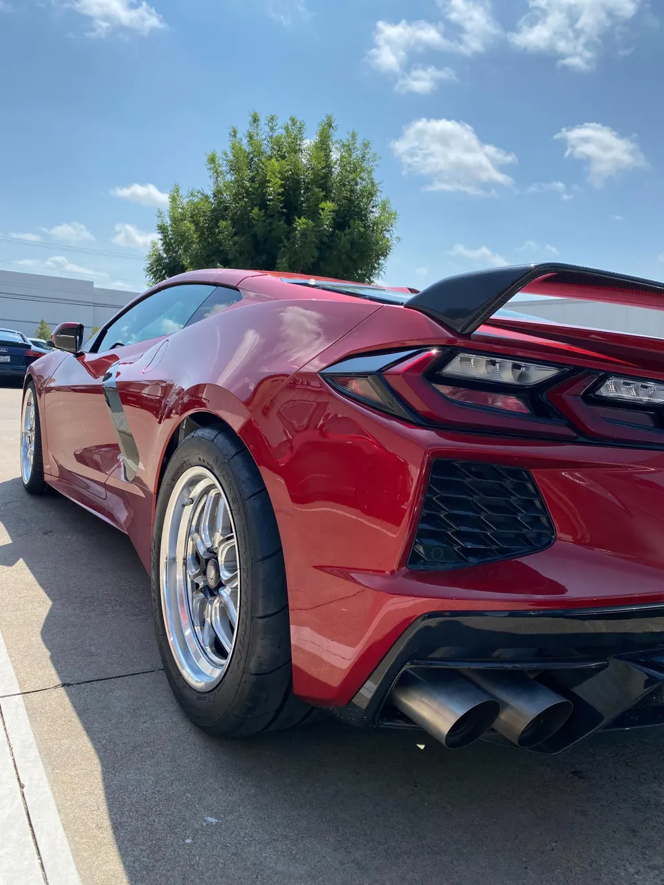 Red C8 Corvette with aftermarket drag wheels, performance tires, and custom exhaust tips parked outdoors.