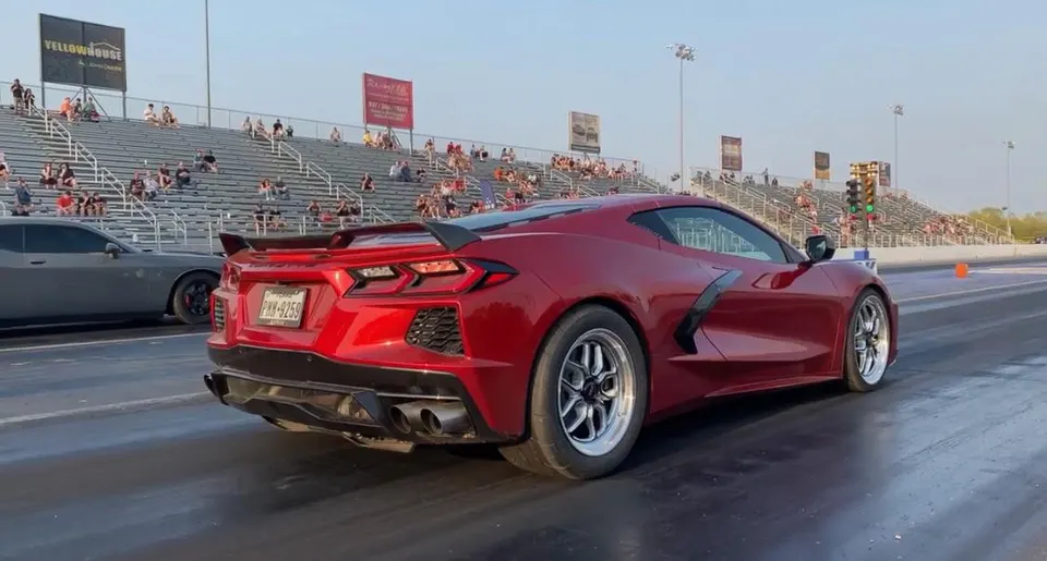 Red C8 Corvette on a drag strip with racing slicks, preparing to launch with grandstands in the background.