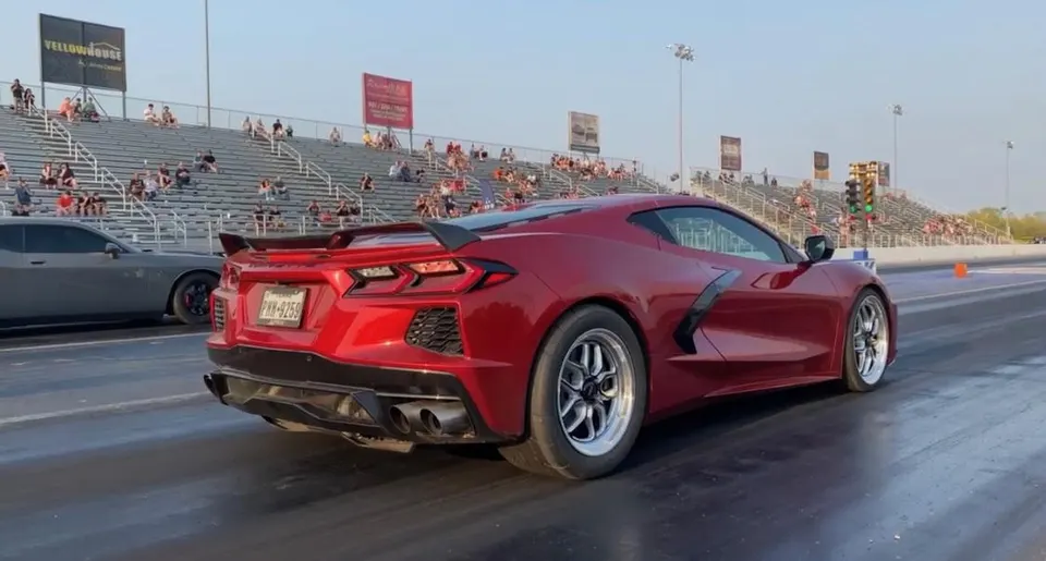 Red Chevrolet Corvette C8 on a drag strip with aftermarket wheels, preparing to race.