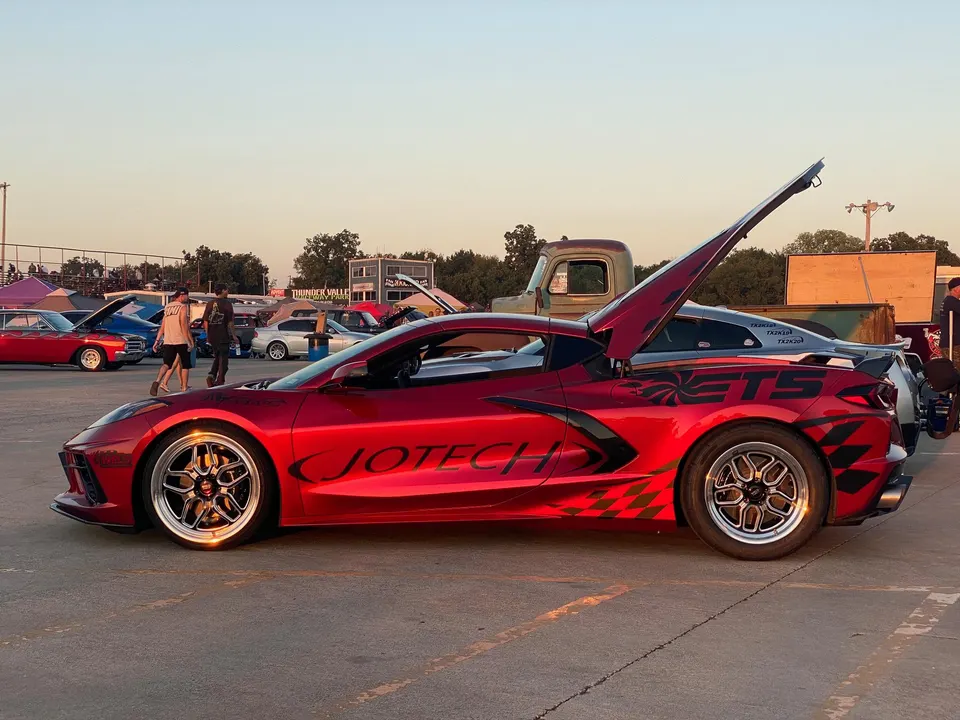 Red Jotech Motorsports Corvette C8.R with aftermarket wheels and graphics, parked at an outdoor car event.