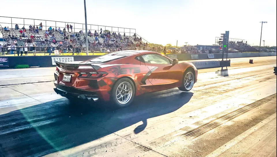 Orange custom wrapped Corvette C8 at a drag strip with spectators in the background, ready to race.