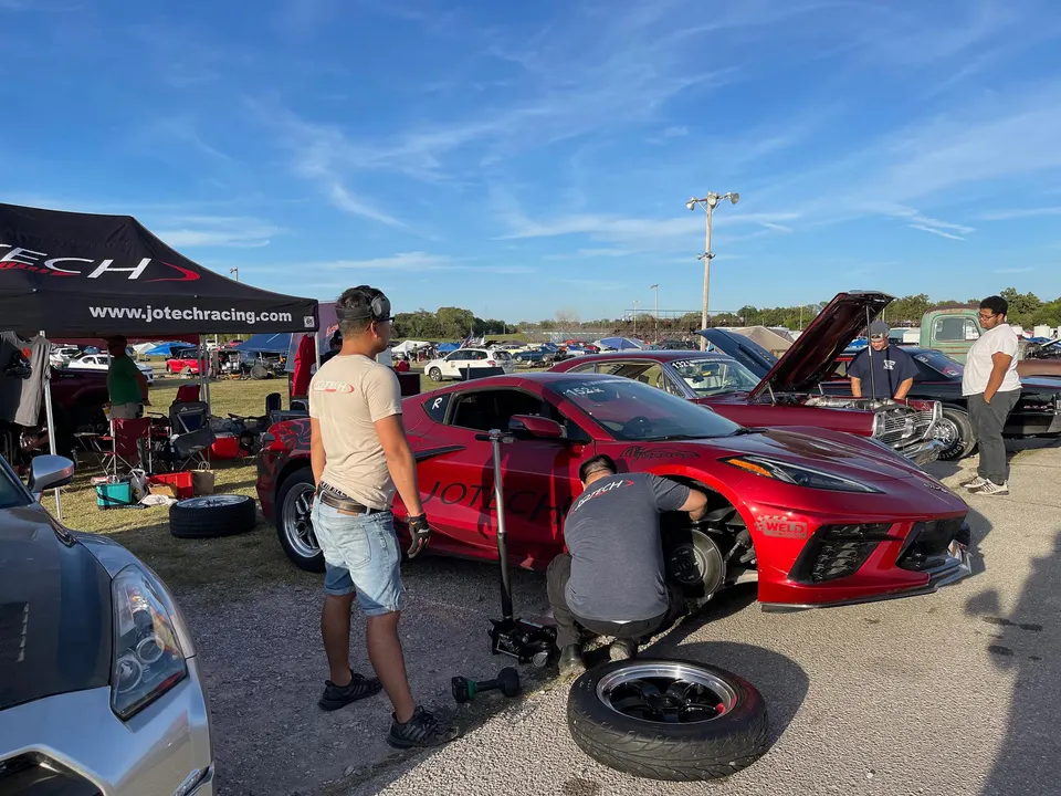 Red Corvette C8 being prepped at a drag racing event, with a mechanic working on the front wheel and brakes.