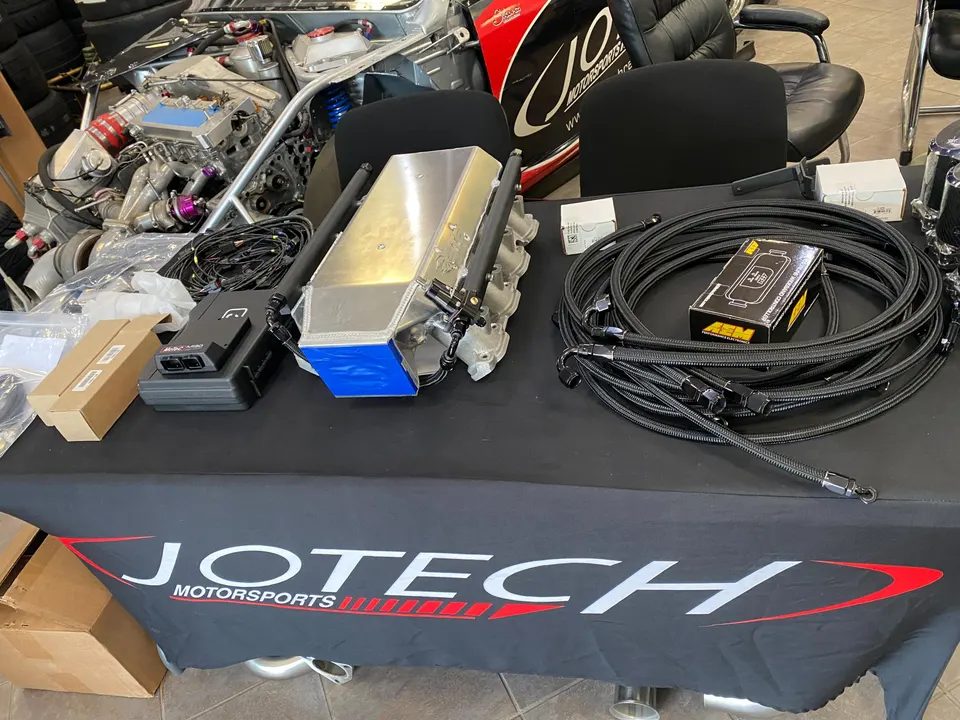 Performance parts laid out on a Jotech Motorsports table, including an intake manifold, fuel lines, Holley EFI, and AEM electronics.
