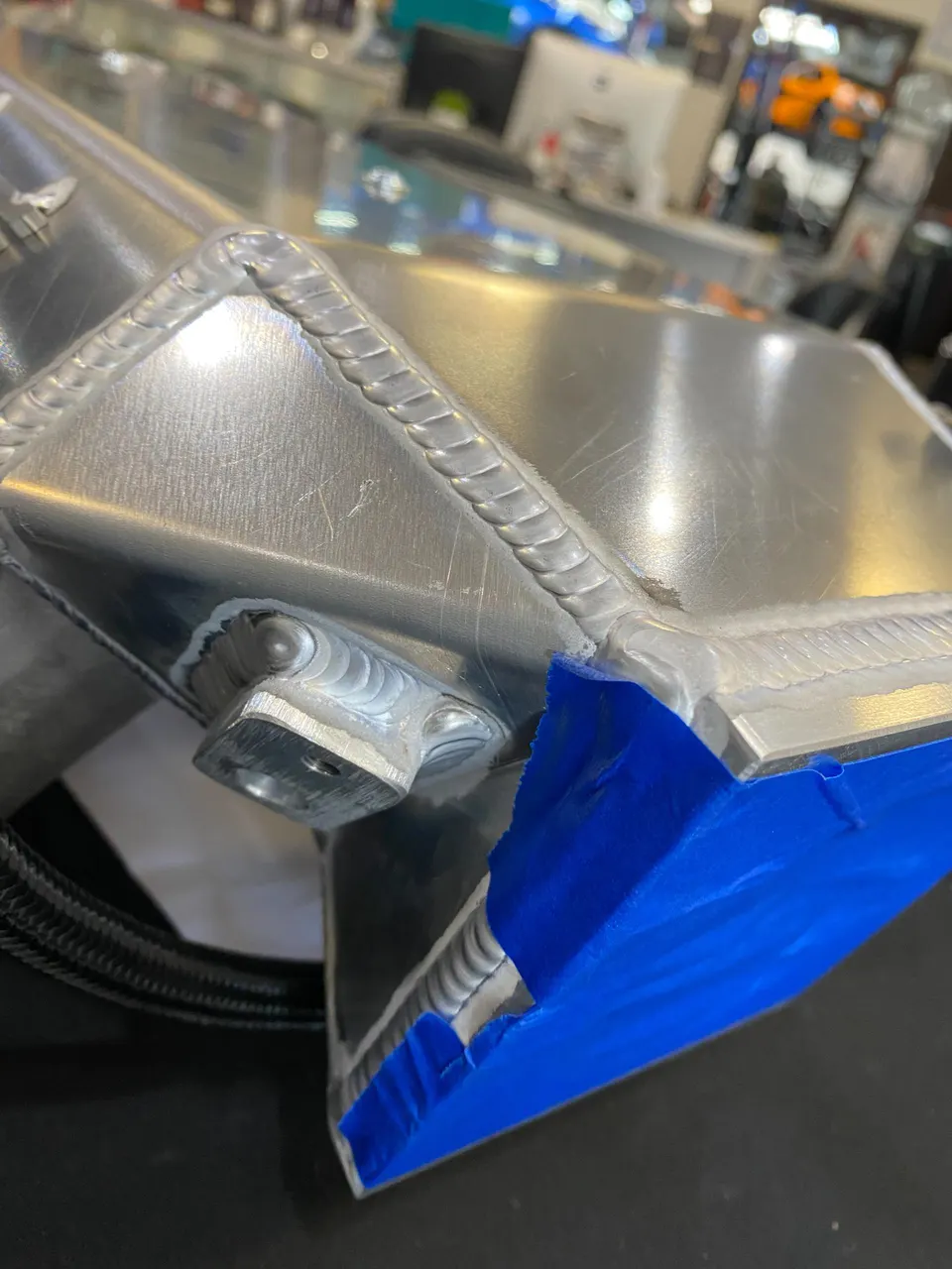 Close-up of custom fabricated aluminum intercooler end tank with visible TIG welds and blue protective tape.