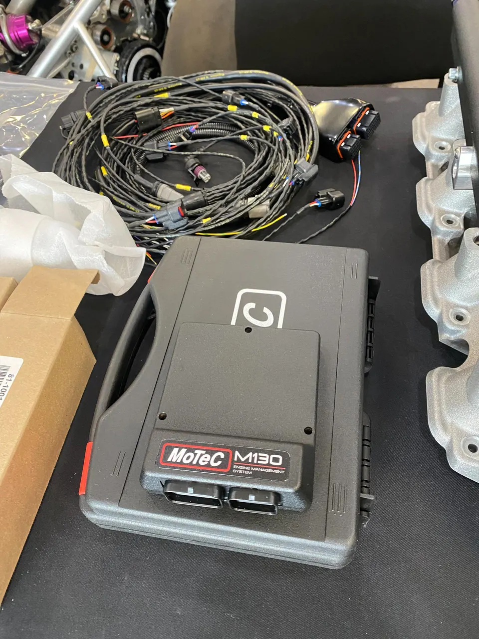 A MoTeC M130 engine management system and wiring harness on a table in a performance shop, ready for installation.