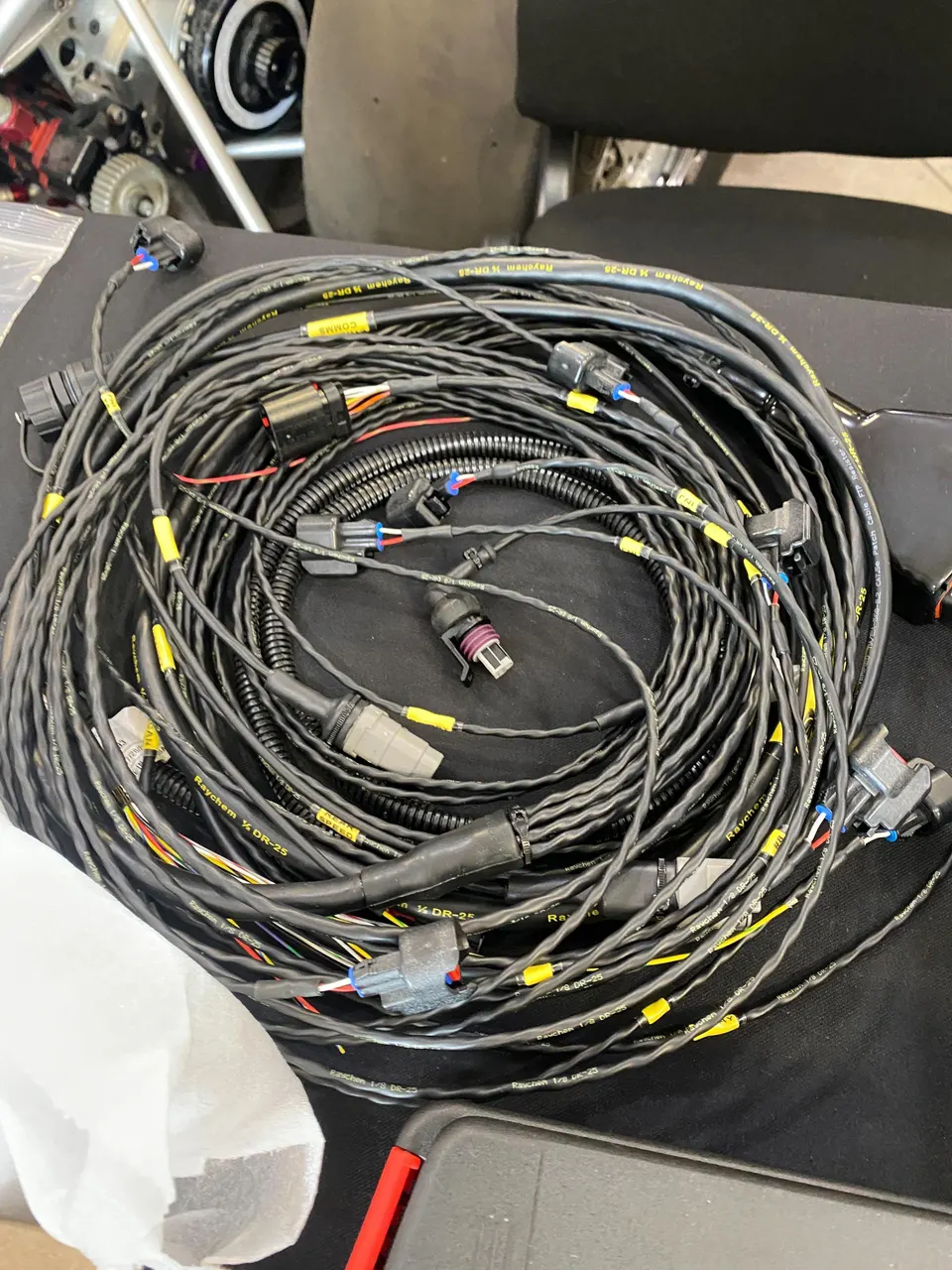 Custom wiring harness with multiple connectors for a high-performance vehicle in a workshop setting.