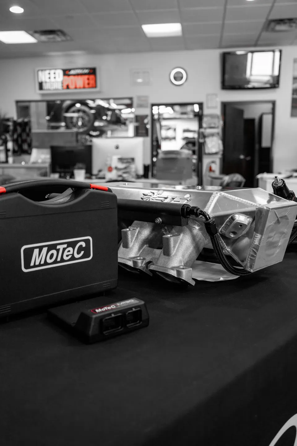 MoTeC ECU and a high-performance intake manifold on a table in a tuning shop, ready for installation.