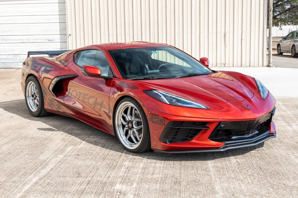 Red Corvette C8.R with aftermarket Weld Racing wheels and a rear wing parked outdoors in front of a building.