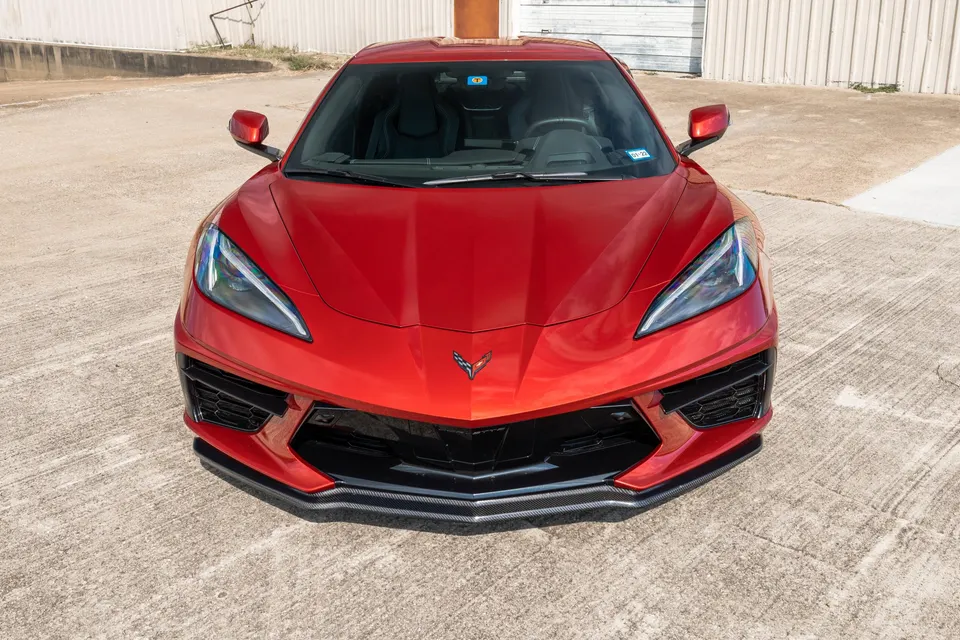 Front view of a red C8 Chevrolet Corvette with a carbon fiber front splitter parked on concrete.