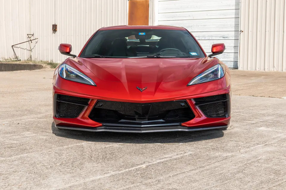 Front view of a red Chevrolet Corvette C8 with a carbon fiber front splitter parked outdoors.