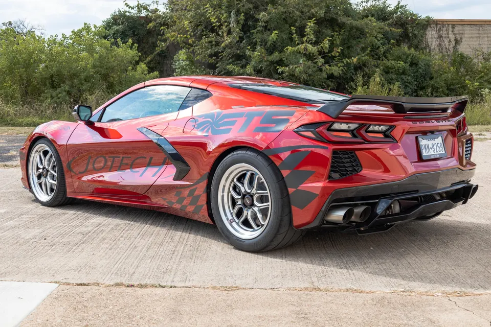 A red C8 Corvette with Jotech Motorsports livery, drag wheels, and a custom exhaust system parked outdoors.
