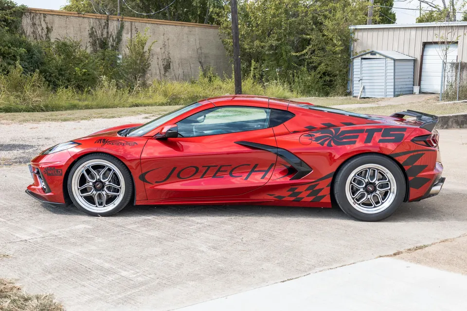 A red Corvette C8.R with custom Jotech Motorsports decals and drag wheels parked outdoors.