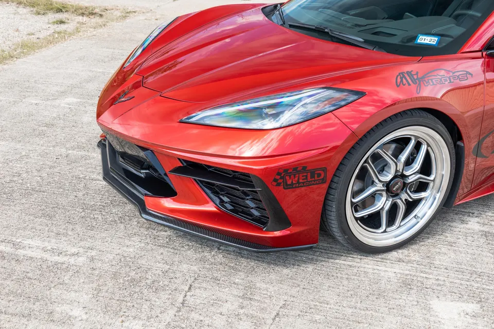 Red C8 Corvette with Weld Racing wheels and a carbon fiber front splitter parked on concrete.