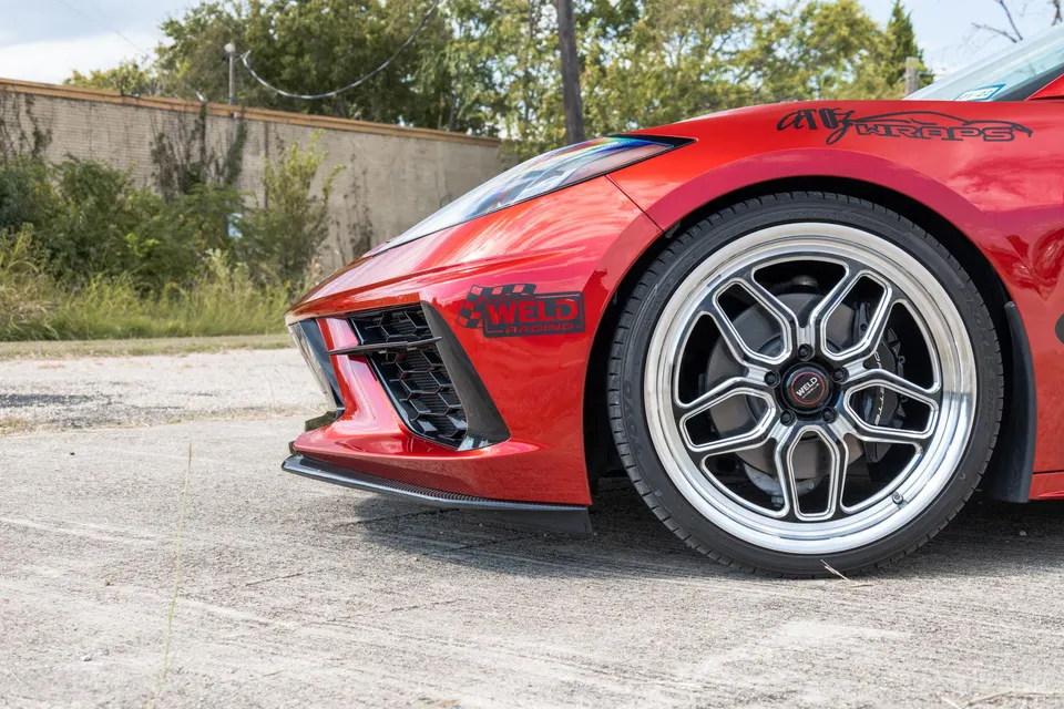 Close-up of a red C8 Corvette's front wheel with Weld Racing drag wheels and a carbon fiber front splitter.