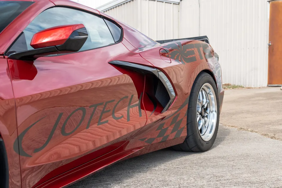 Red Corvette C8.R with Jotech graphics, drag racing wheels, and side air intake, parked outdoors.