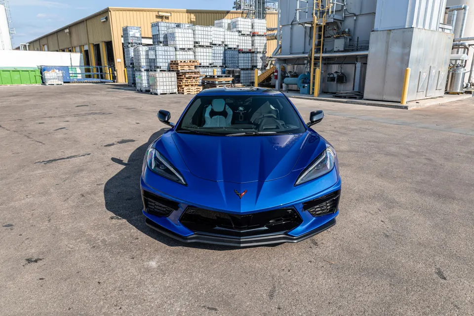 Front view of a blue Chevrolet Corvette C8 parked in an industrial area on a sunny day.